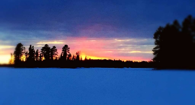 The sky appears in gentle colors above trees and a snowy landscape
